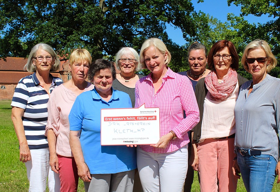 Ehrenamtliche Helfer des DRK halten Tafel mit Spendenaufruf